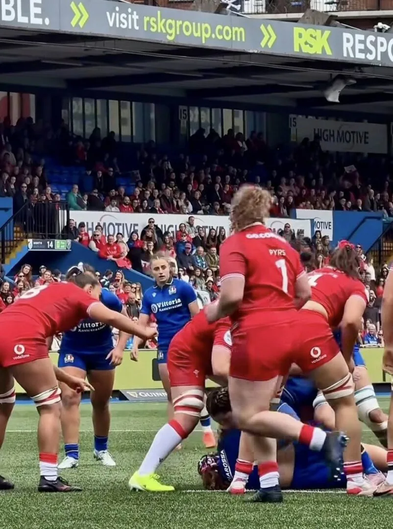 Giocatrici delle nazionali femminili di rugby di Italia e Galles durante una fase di gioco ravvicinata vicino alla linea laterale del campo.