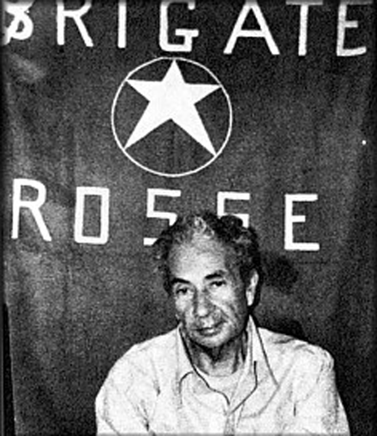 Fotografia storica in bianco e nero di Aldo Moro seduto davanti alla bandiera delle Brigate Rosse durante il sequestro del 1978.