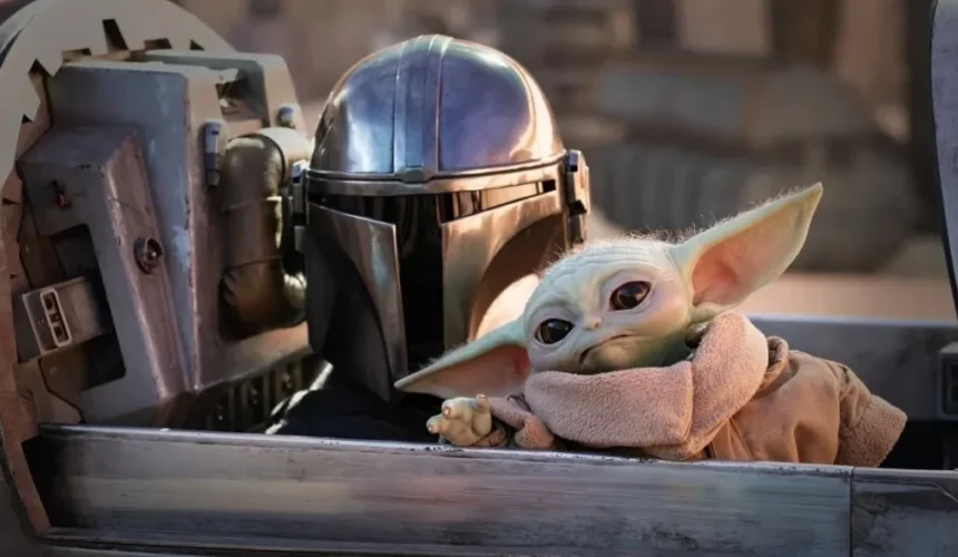 Il Mandaloriano con armatura argentata accanto a Grogu, detto Baby Yoda, seduti a bordo di un veicolo nell’universo di Star Wars.