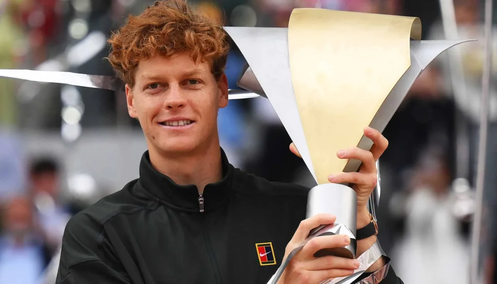 Il tennista Jannik Sinner tiene in mano il trofeo del torneo di Madrid mentre sorride davanti ai fotografi.