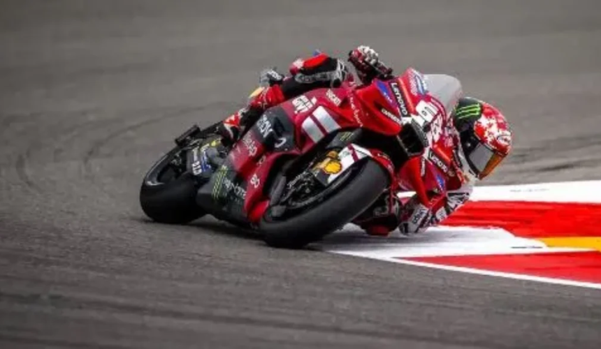 Pilota di MotoGP su una moto Ducati rossa affronta una curva del circuito con una piega molto accentuata vicino al cordolo.
