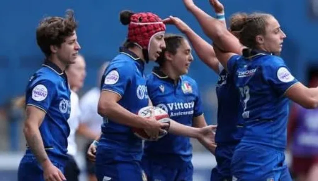 Giocatrici della nazionale italiana femminile di rugby in maglia azzurra durante una partita, con una atleta che tiene il pallone in mano.