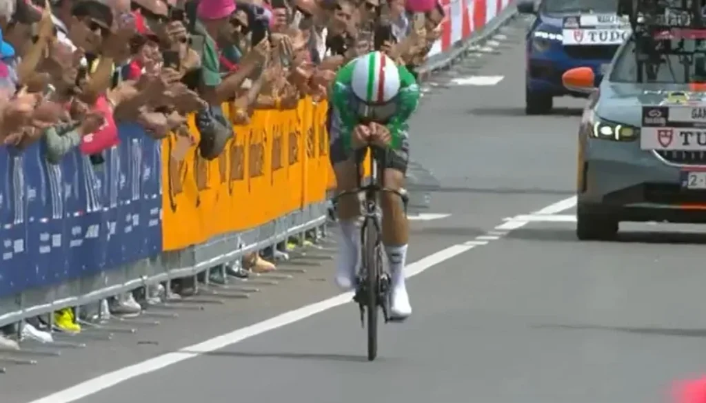 Il ciclista italiano Filippo Ganna pedala in posizione aerodinamica durante una cronometro con il pubblico ai lati della strada.