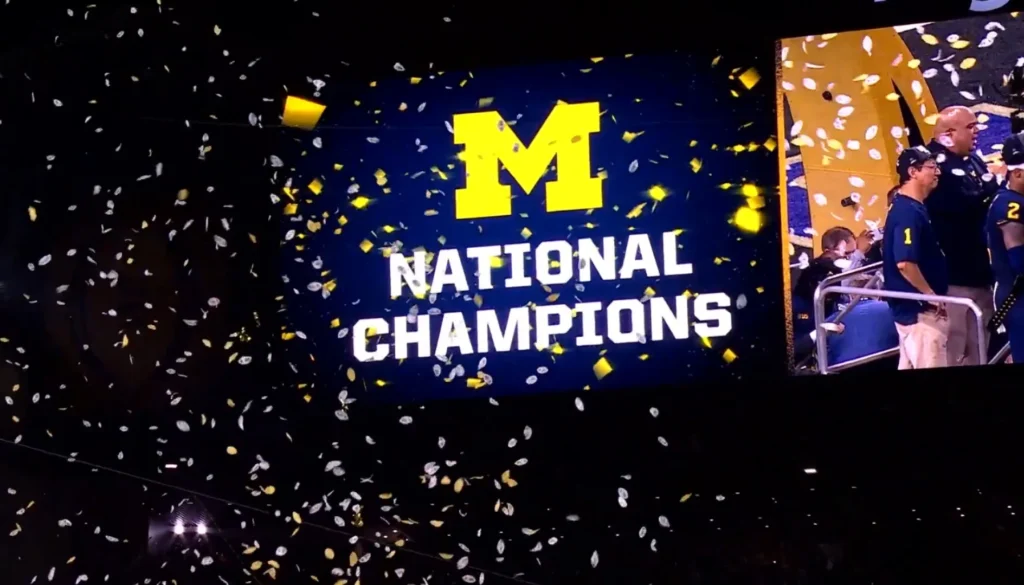 Maxischermo con la scritta “National Champions” dei Michigan Wolverines circondato da coriandoli durante i festeggiamenti per la vittoria del titolo.
