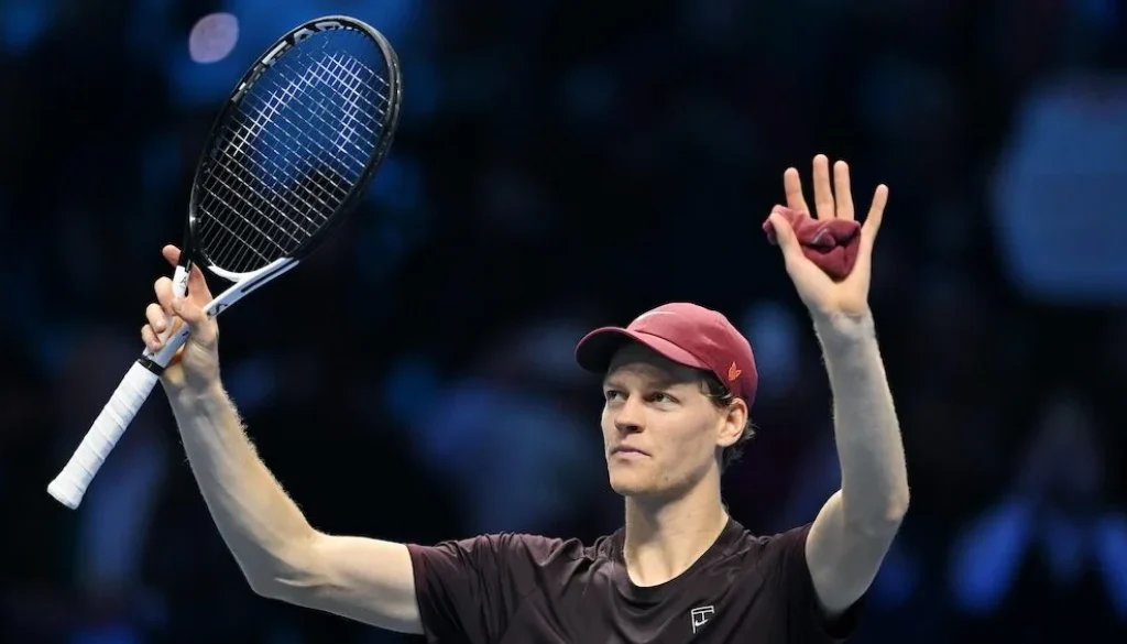 Il tennista Jannik Sinner alza la racchetta e saluta il pubblico durante un match indoor a Torino.