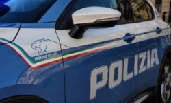 Primo piano di un'auto della Polizia di Stato italiana con la scritta "Polizia" ben visibile sulla fiancata, in un contesto urbano.