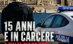 Un ragazzo di spalle con le mani ammanettate osserva il lungomare di Malta, mentre in primo piano è presente un'auto della polizia maltese. L'immagine rappresenta il caso del 15enne italiano arrestato sull'isola.